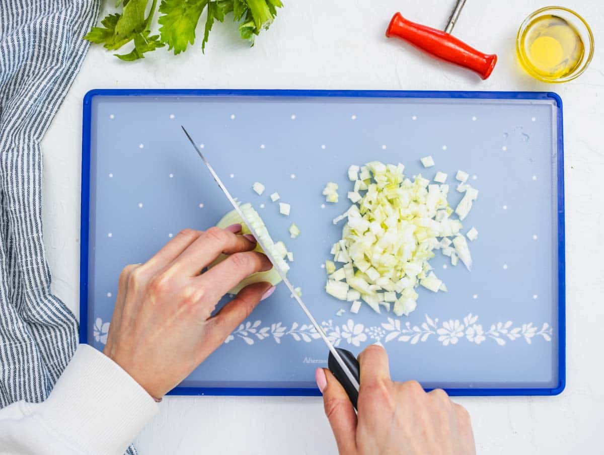 female hands chopping white onion on a cutting board