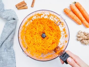 carrots grated in a food processor with hand holding the handle