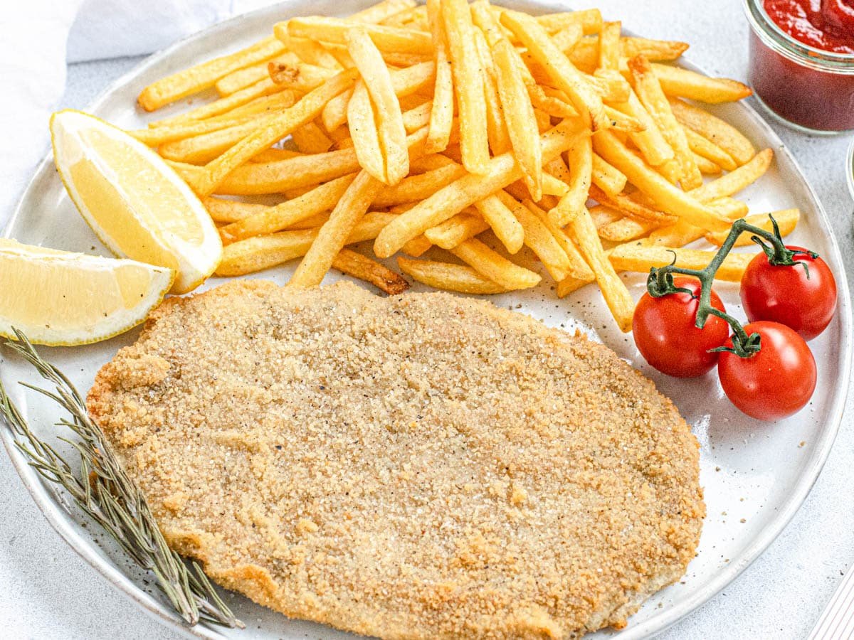 Vegan schnitzel on a plate with fries and lemon wedges