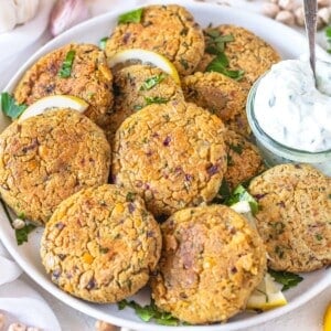 chickpea fritters on a platter with lemon wedges and tzatziki sauce