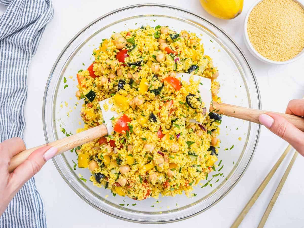 hands mixing couscous salad in a glass bowl