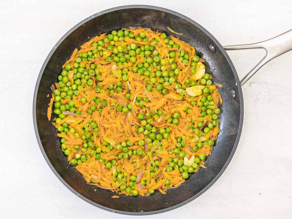 black skillet with peas and grated carrots
