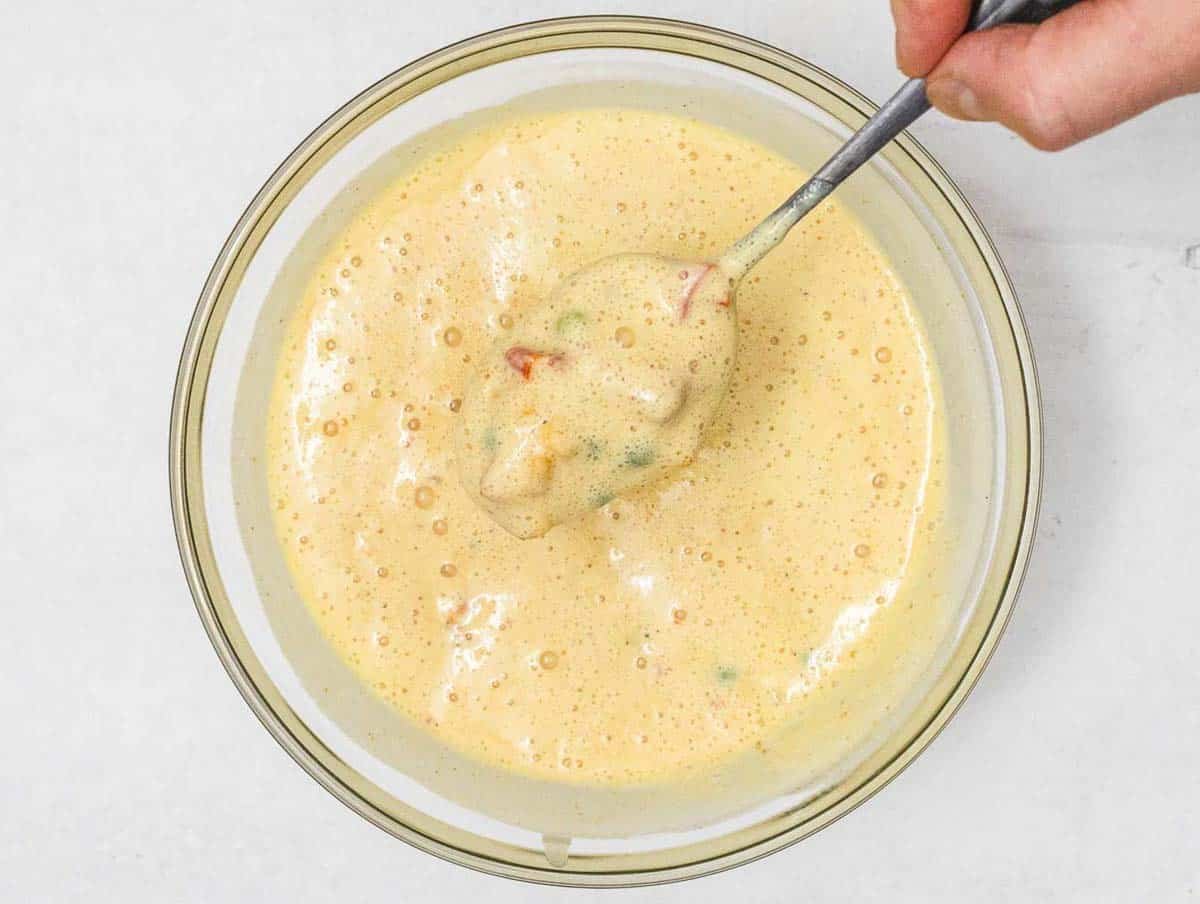 Chickpea Muffin batter with veggies and hand holding a spoon