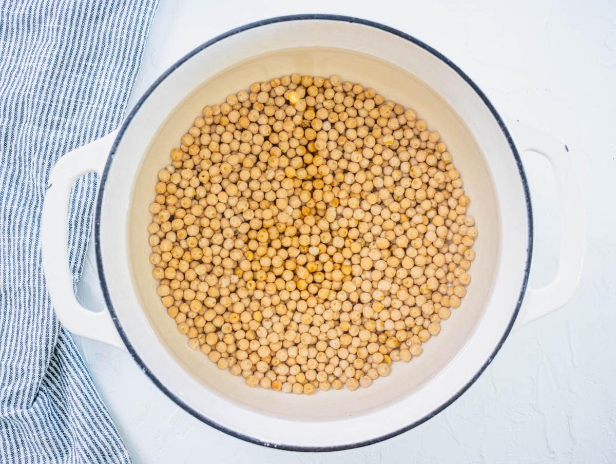 small dried chickpeas soaking overnight in a white pot