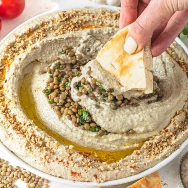 Lentil hummus on a white plate with fresh parsley and hand holding a pita