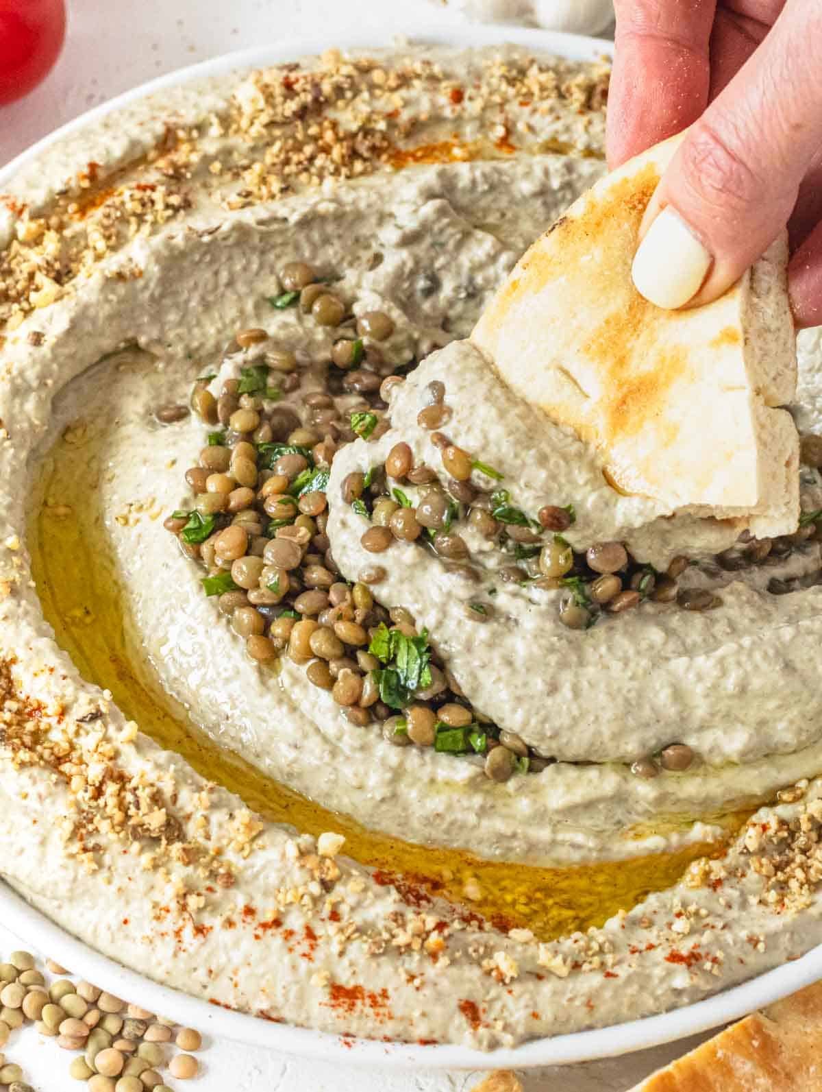 Lentil hummus with hand holding a piece of pita