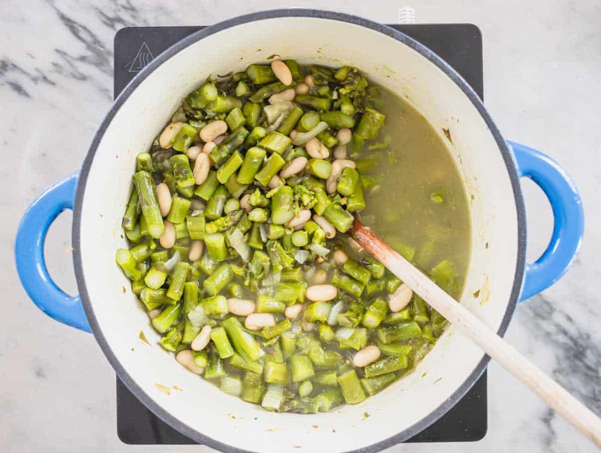 Asparagus soup and cannellini beans with a wooden spoon in a pot