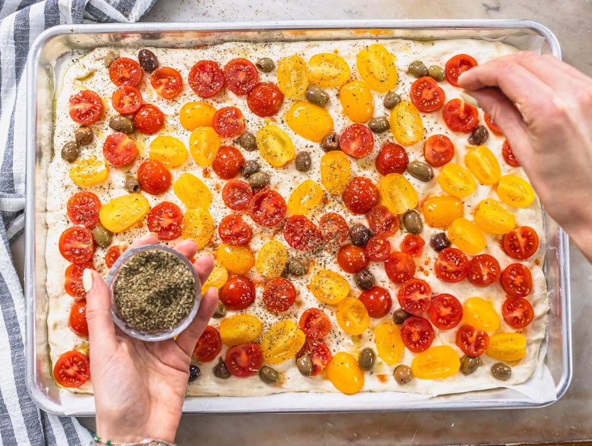 hands with oregano and a focaccia pizza