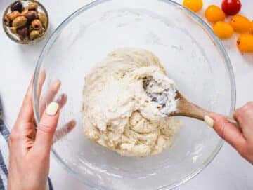 hands with a wooden spoon mixing dough in a glass bowl