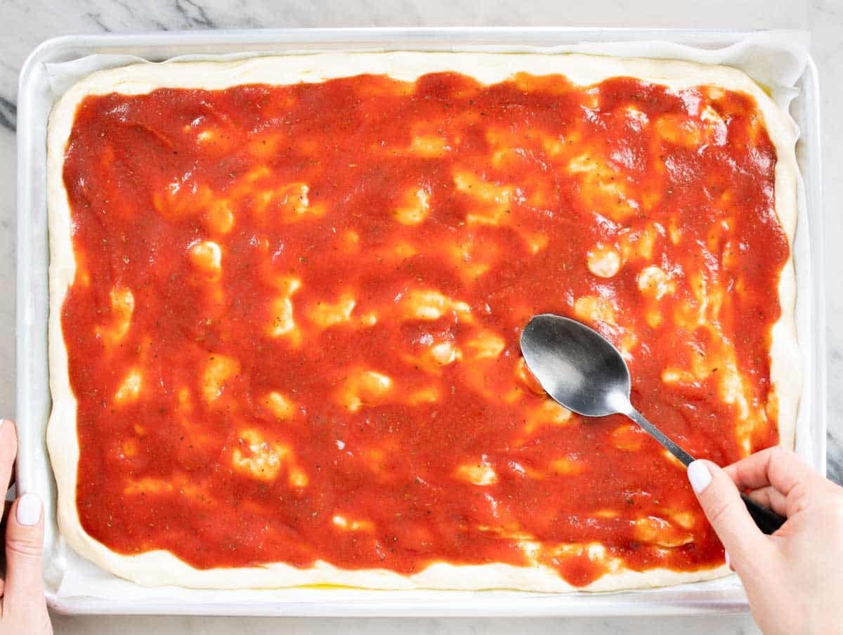 hands spreading tomato sauce with a black spoon