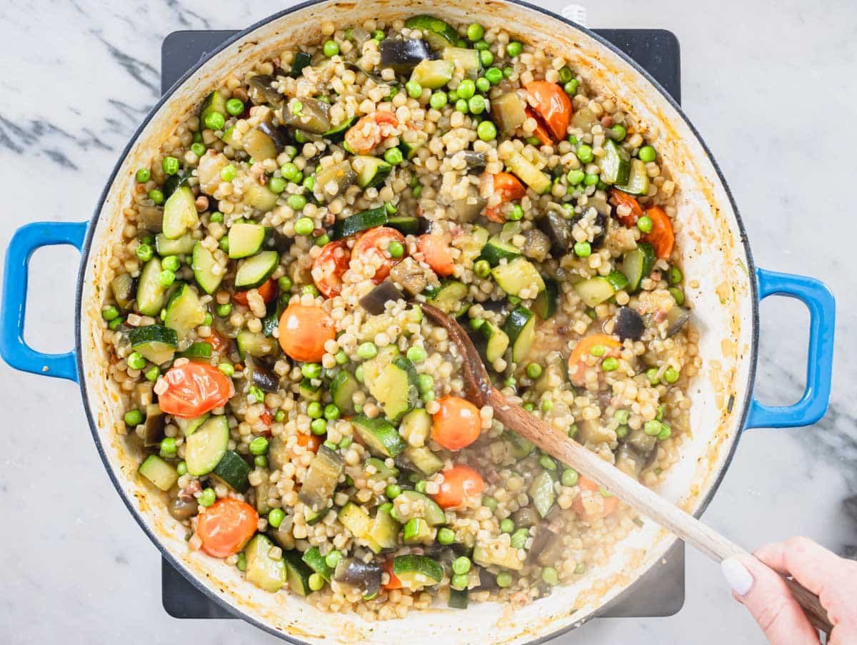 hand cooking vegetables and fregula in a skillet