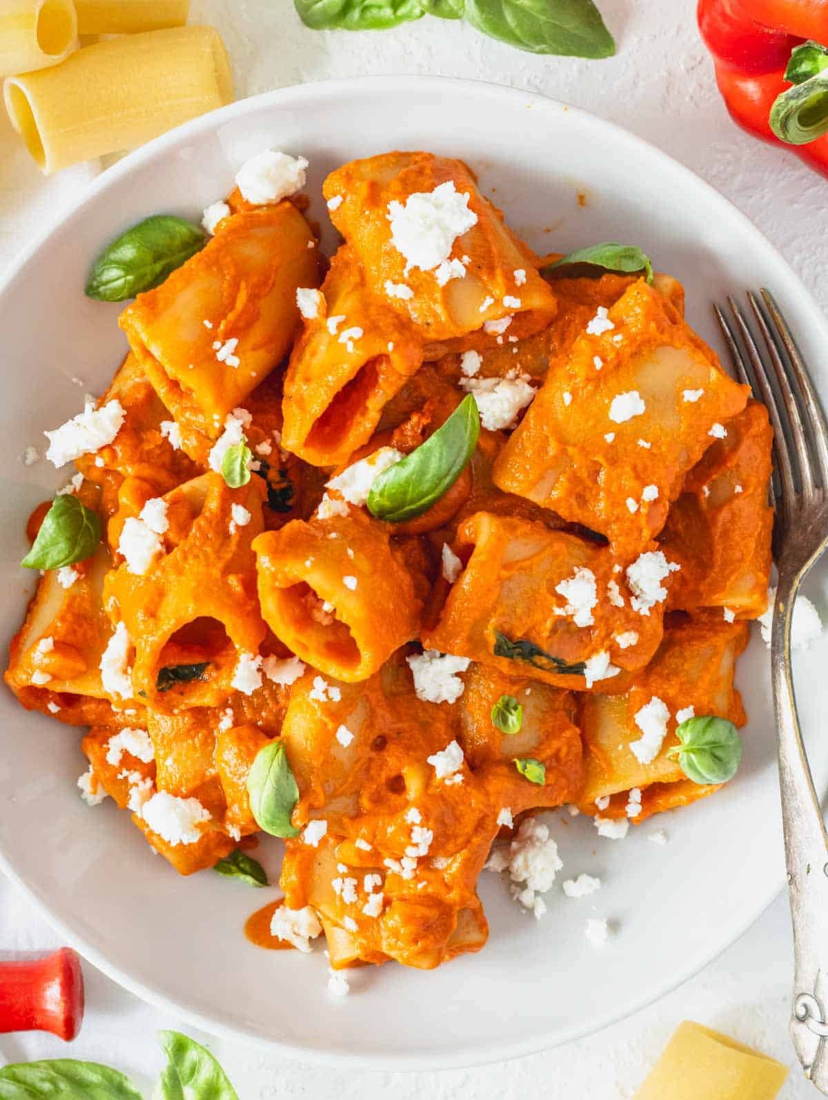 High protein pasta with feta crumble and fresh basil leaves in a white bowl