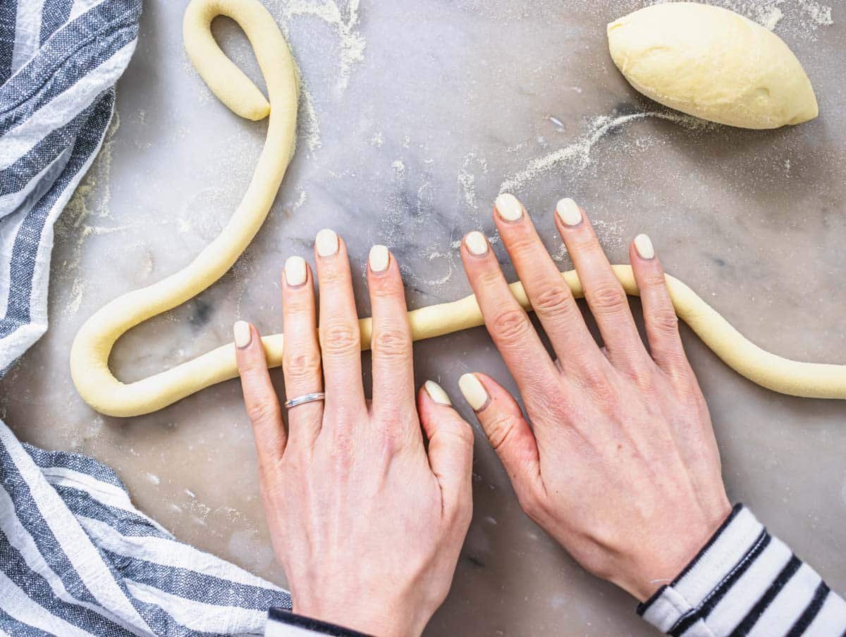 Hands rolling a rope of pasta dough on marble