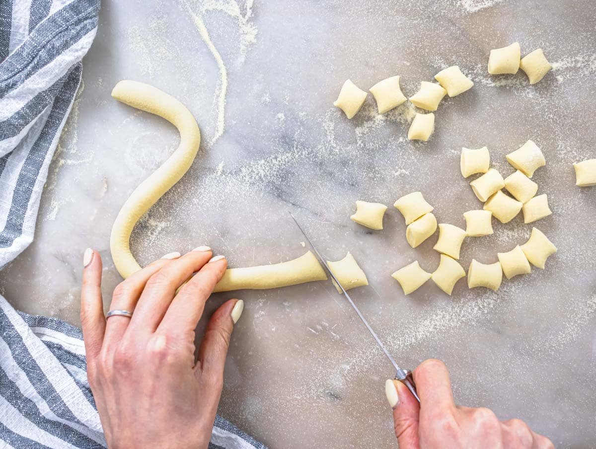 Hands cutting pasta dough into small pieces