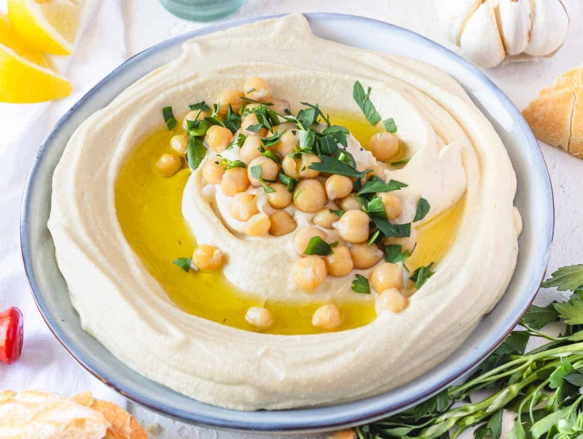 Hummus recipe on a plate with lemon and pita bread on the side
