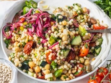 Israeli couscous with fresh vegetables on a white plate with a fork