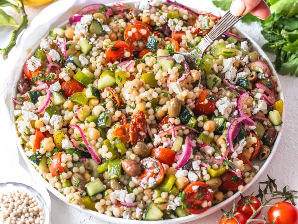 Israeli couscous salad on a big white plate with a silver spoon