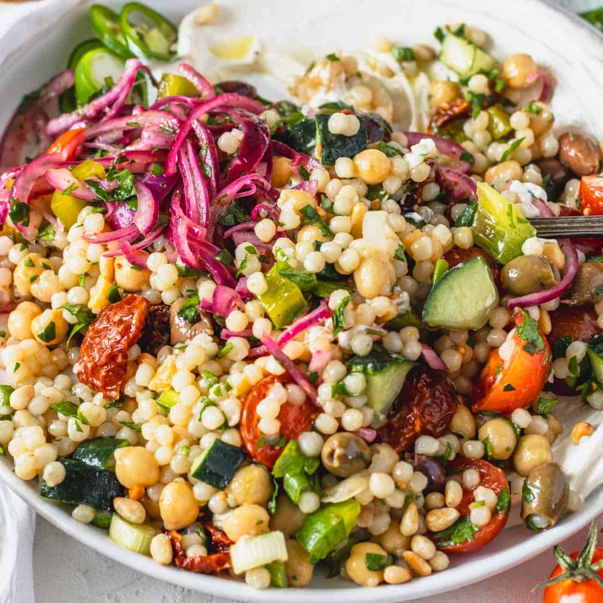 Israeli salad with sumac onions and pearl couscous on a white plate