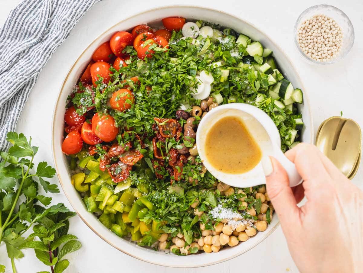 hand with dressing drizzling over Israeli couscous 