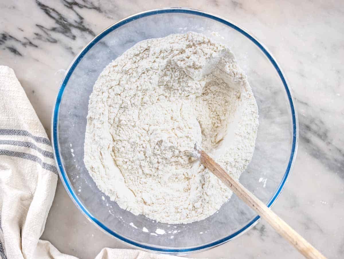 flour in a glass bowl with a wooden spoon