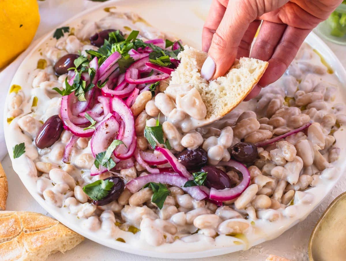 Piyaz on a white plate with hand holding a pita