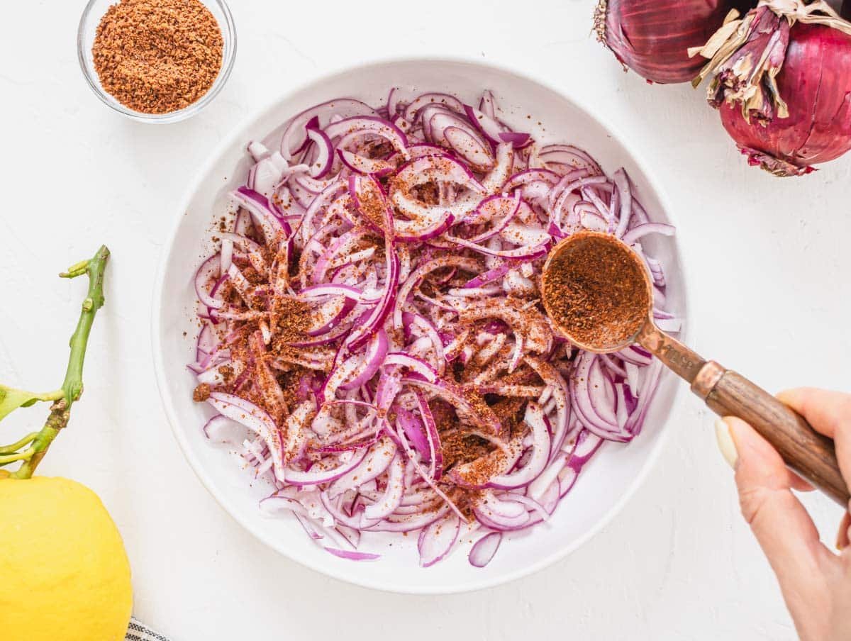 sliced red onions in a white bowl with sumac