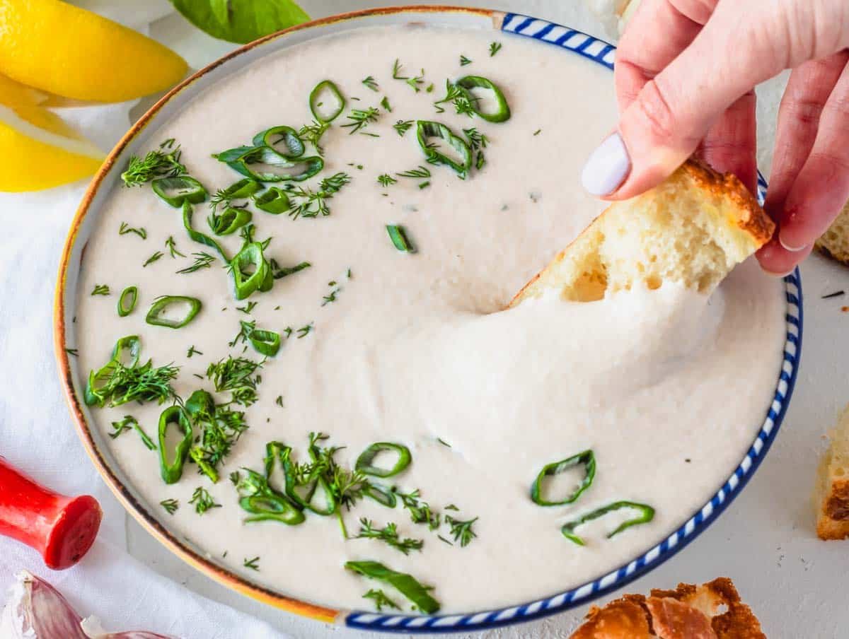 White bean dip in a bowl and hand holding a focaccia