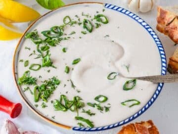 White bean dip in a bowl with scallions and a silver spoon
