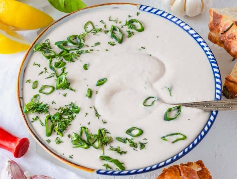 White bean dip in a bowl with scallions and a silver spoon