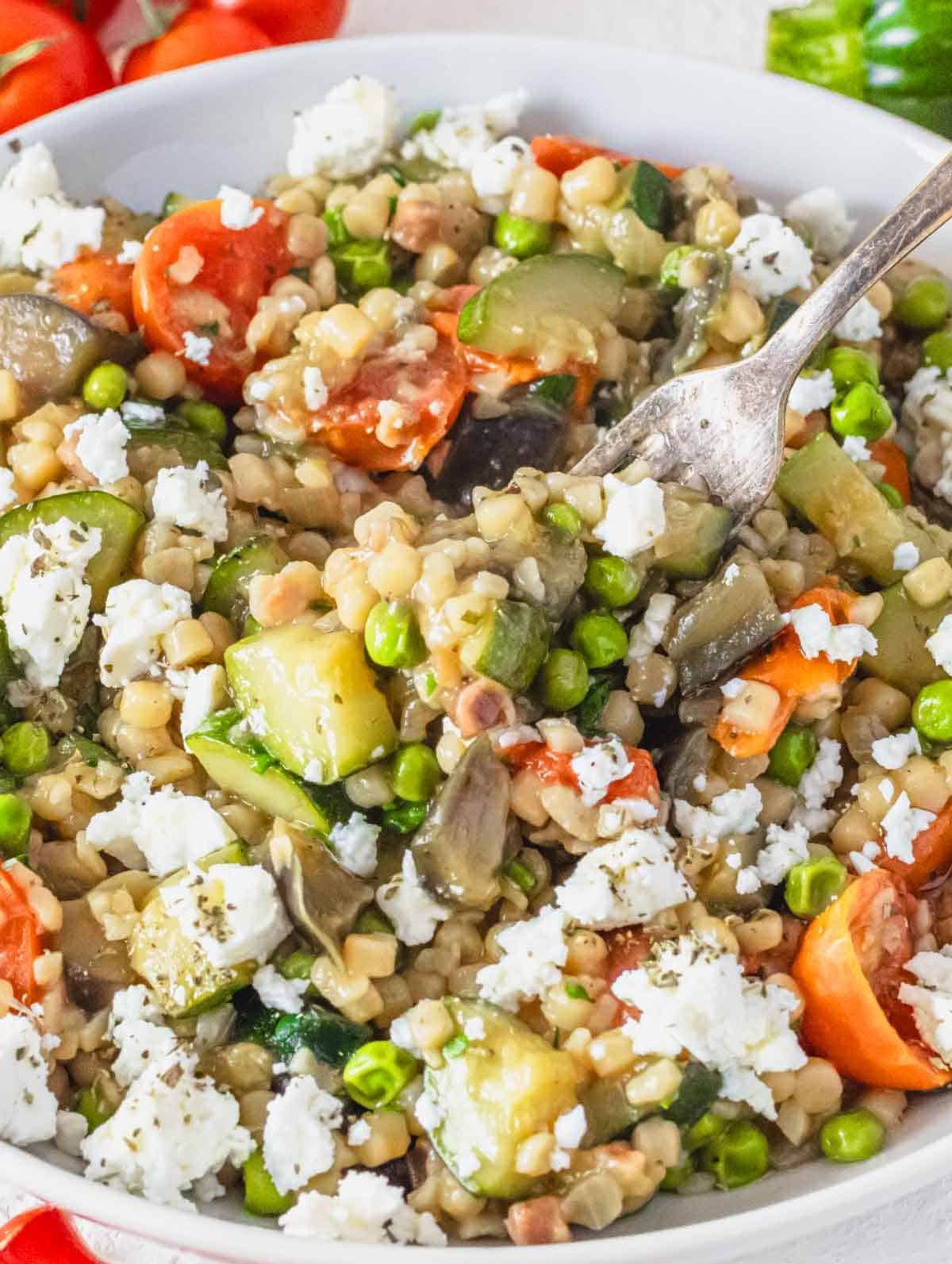 Creamy fregola with vegetables and a silver fork