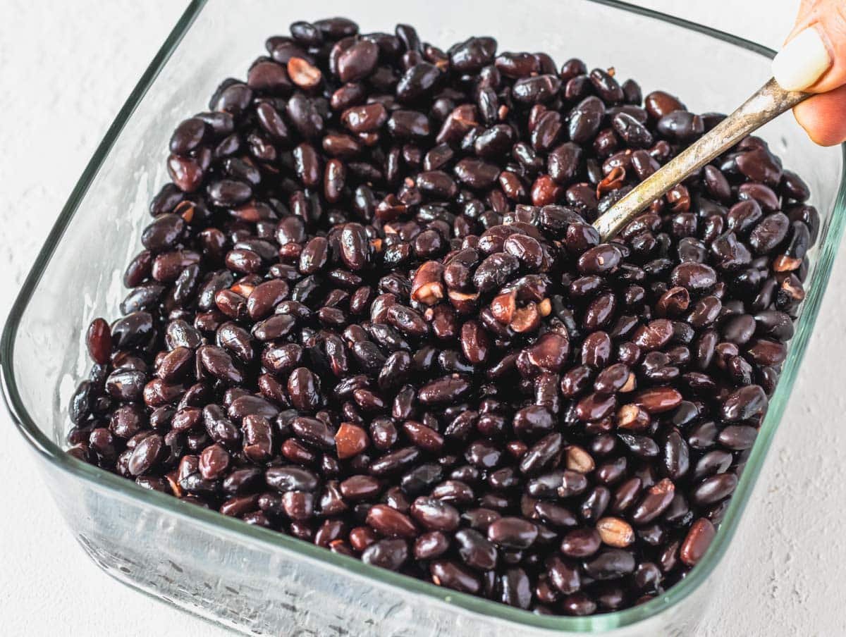 black beans in a see-through glass container with a spoon