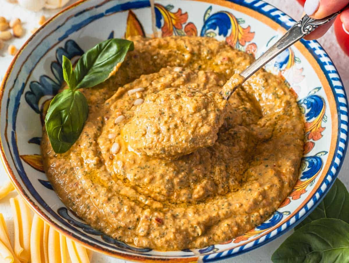 red tomato pesto in a blue bowl with a silver spoon