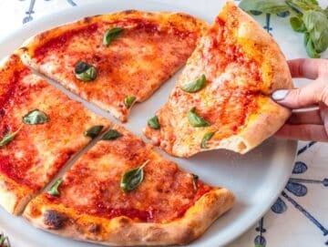 Louise grabbing a slice of baked pizza with tomato and cheese