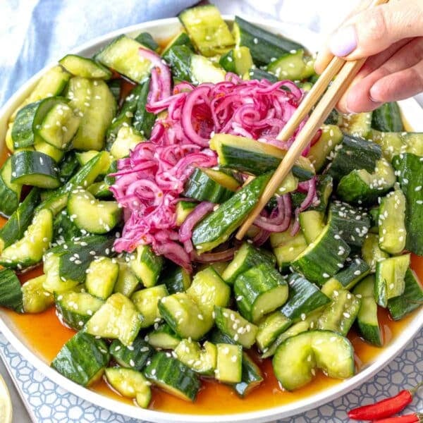 Asian cucumber salad with hands holding chopsticks and taking a cucumber