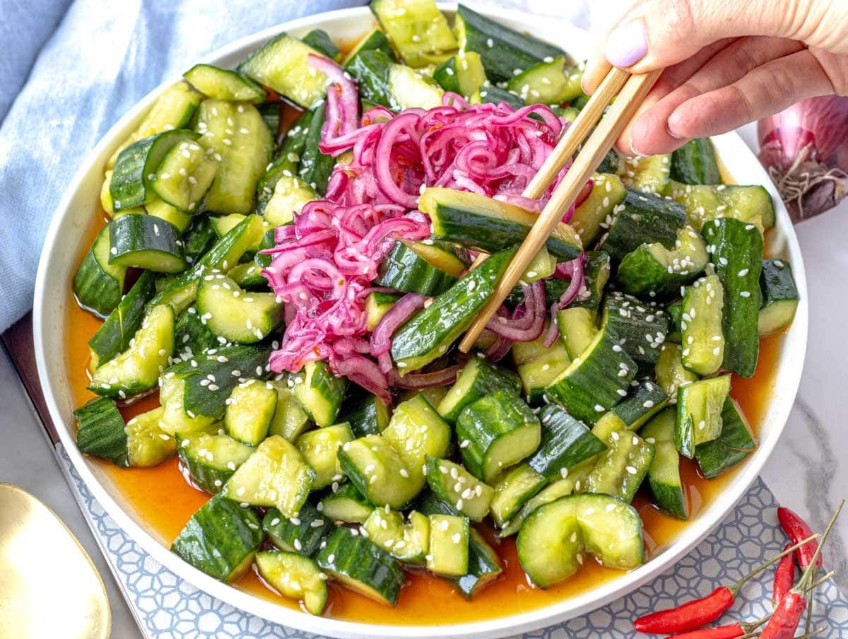Asian cucumber salad with hands holding chopsticks
