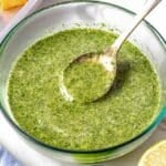 Cilantro lime dressing in a glass bowl with a silver spoon and a blue cloth
