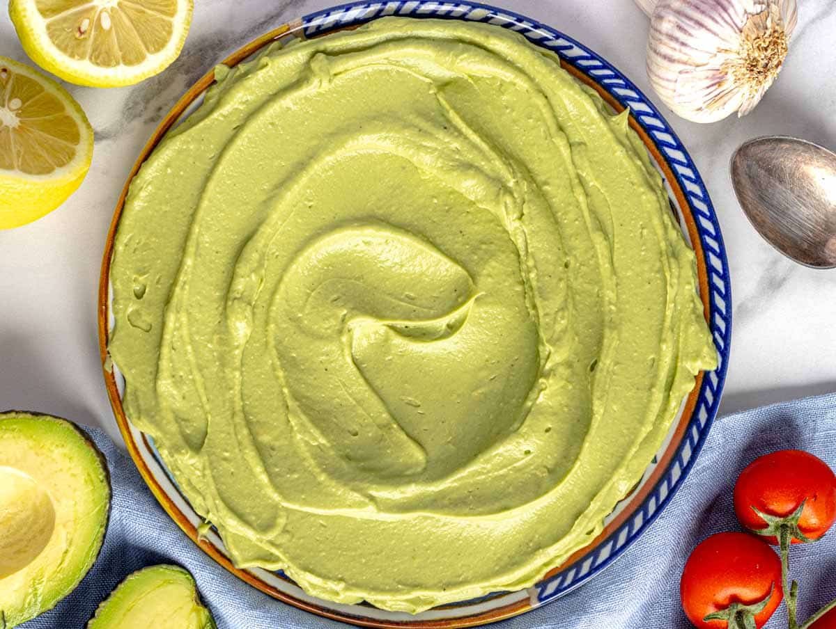 Creamy Avocado spread on a blue plate with tomatoes and lemon on the side