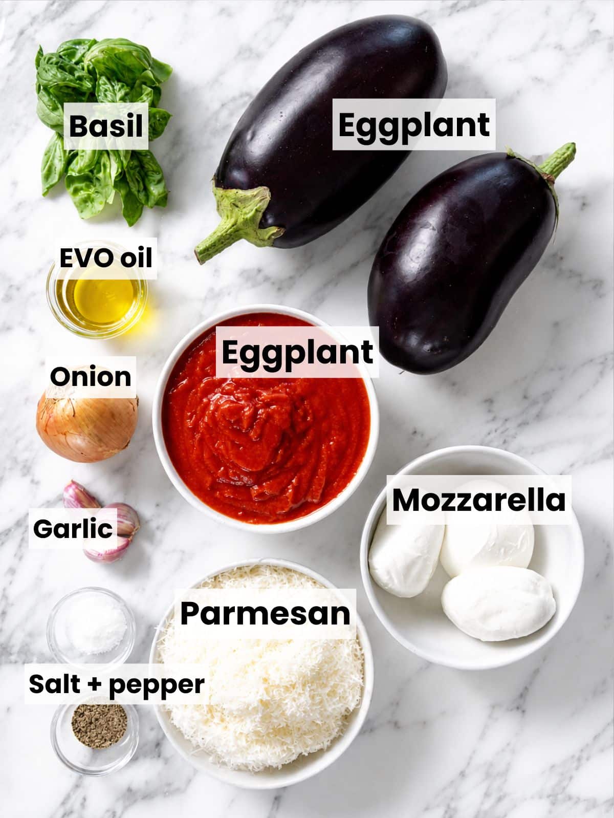 Ingredients for Eggplant Parmigiana arranged on white marble in natural window light.