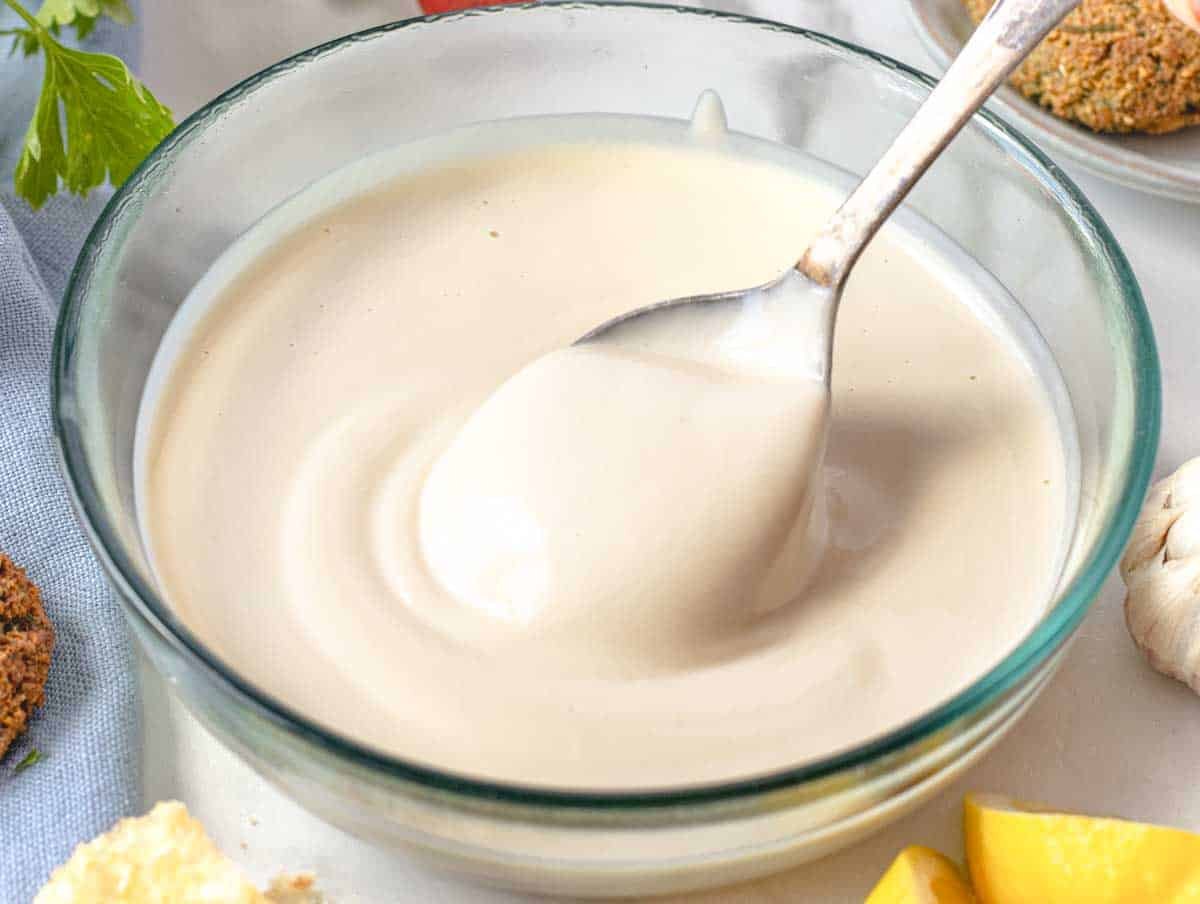 Creamy tahini sauce in a glass bowl with a silver spoon