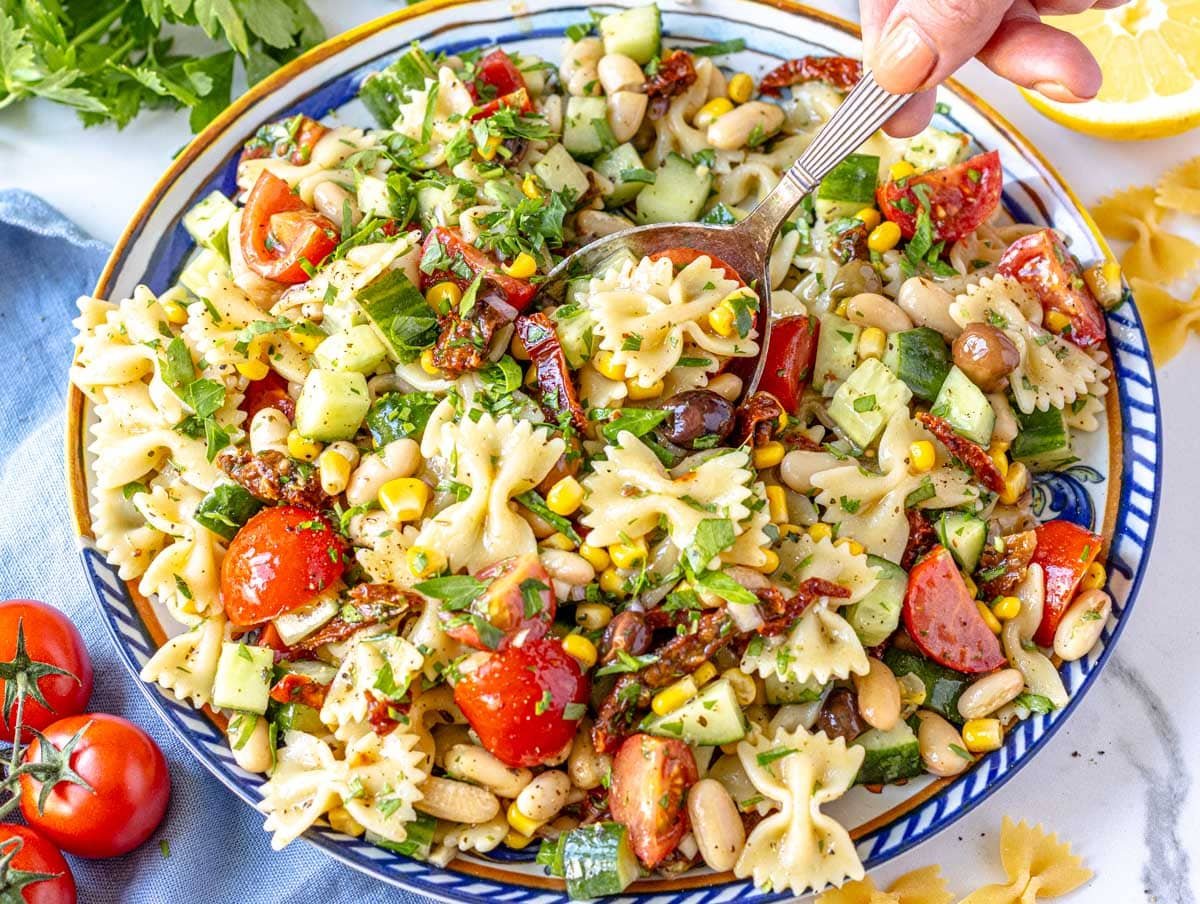 Vegan Pasta Salad on a blue plate with hand holding a silver spoon