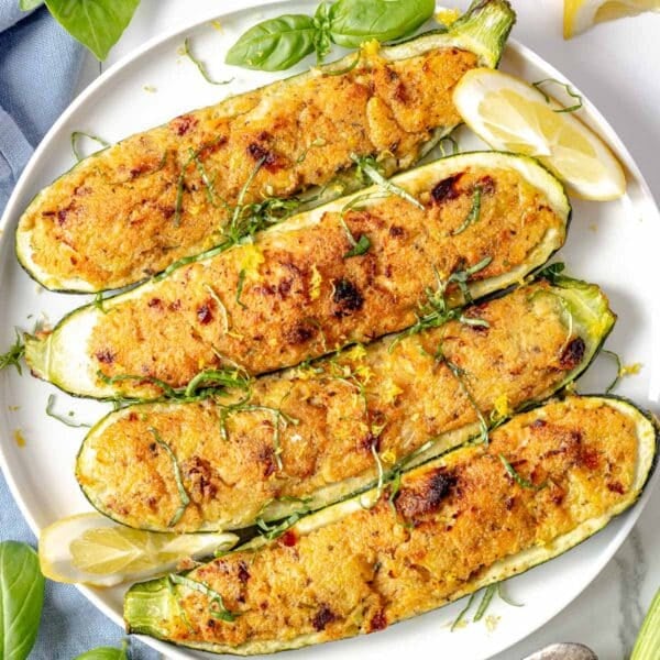 stuffed zucchini with fresh basil and lemon wedges on a white plate