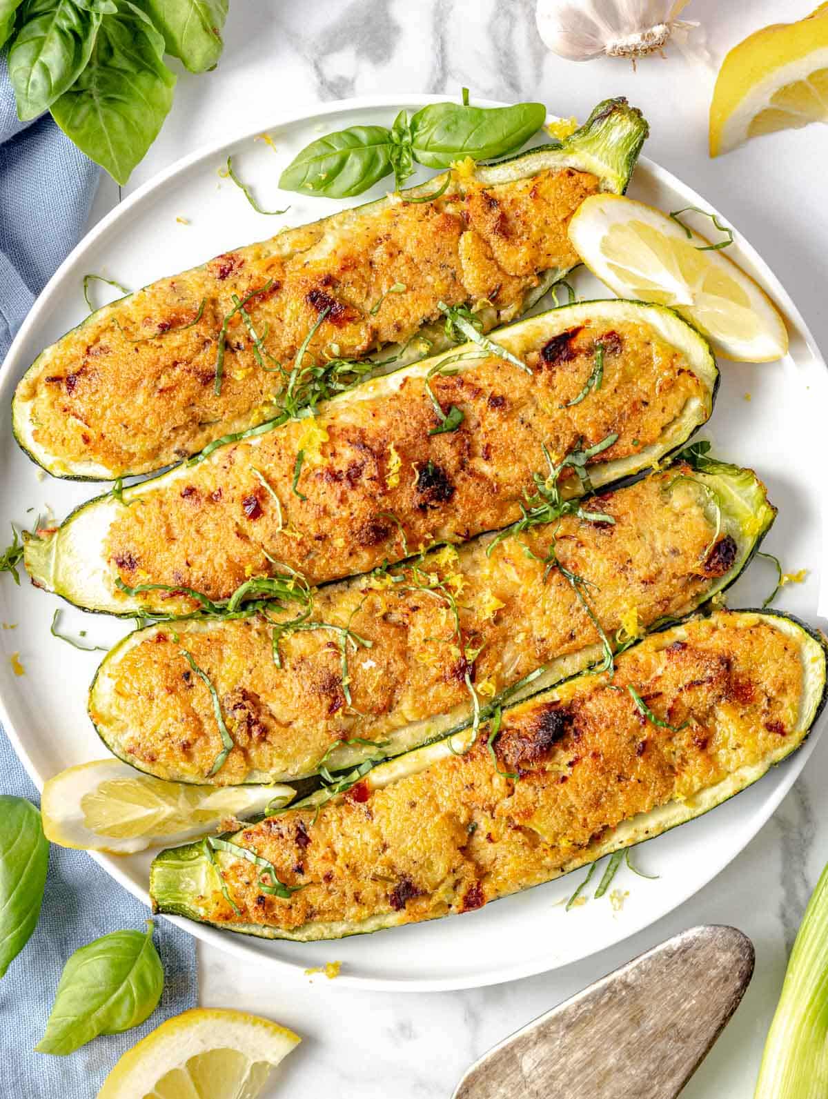 stuffed zucchini on a plate with fresh basil and lemon wedges