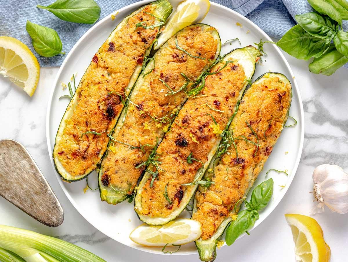 stuffed zucchini on a white plate with fresh herbs and lemon on the side