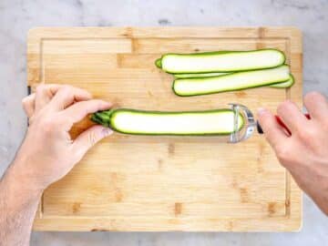 hands shaving zucchini on a cutting board