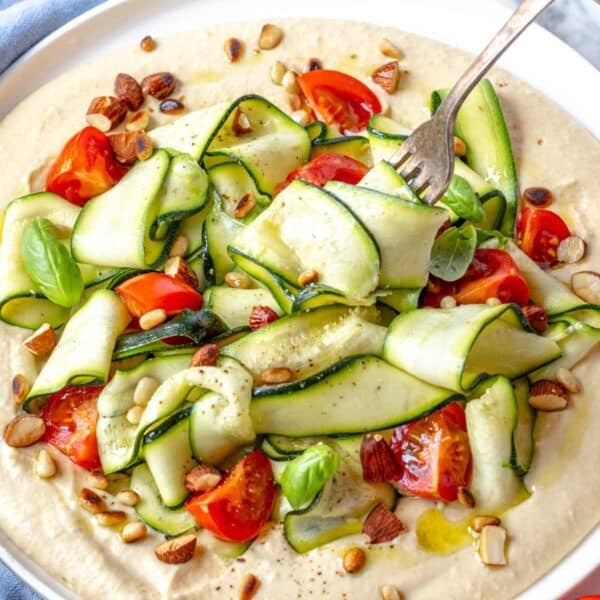 zucchini salad with toasted nuts on hummus served with a fork
