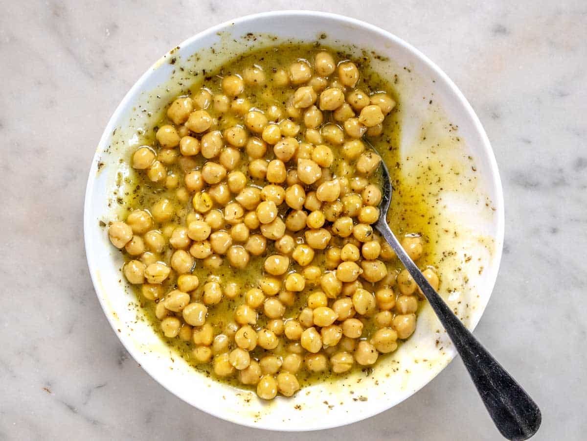 Chickpeas marinating in a white bowl with a black spoon
