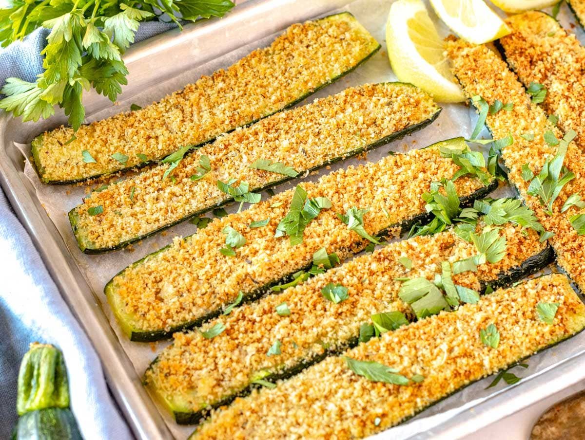 Roasted zucchini on a silver tray with lemon wedges