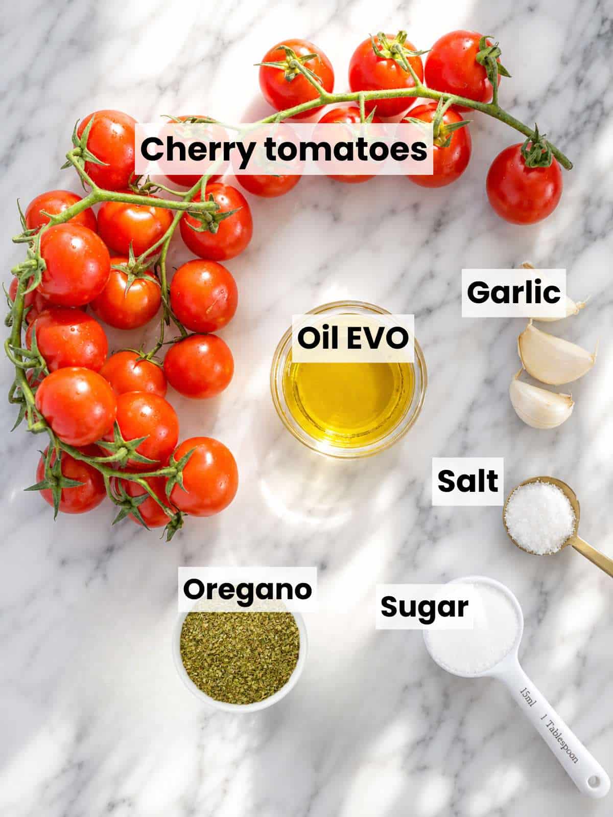 Tomato confit ingredients on white marble with cherry tomatoes, garlic, dried herbs, and olive oil.