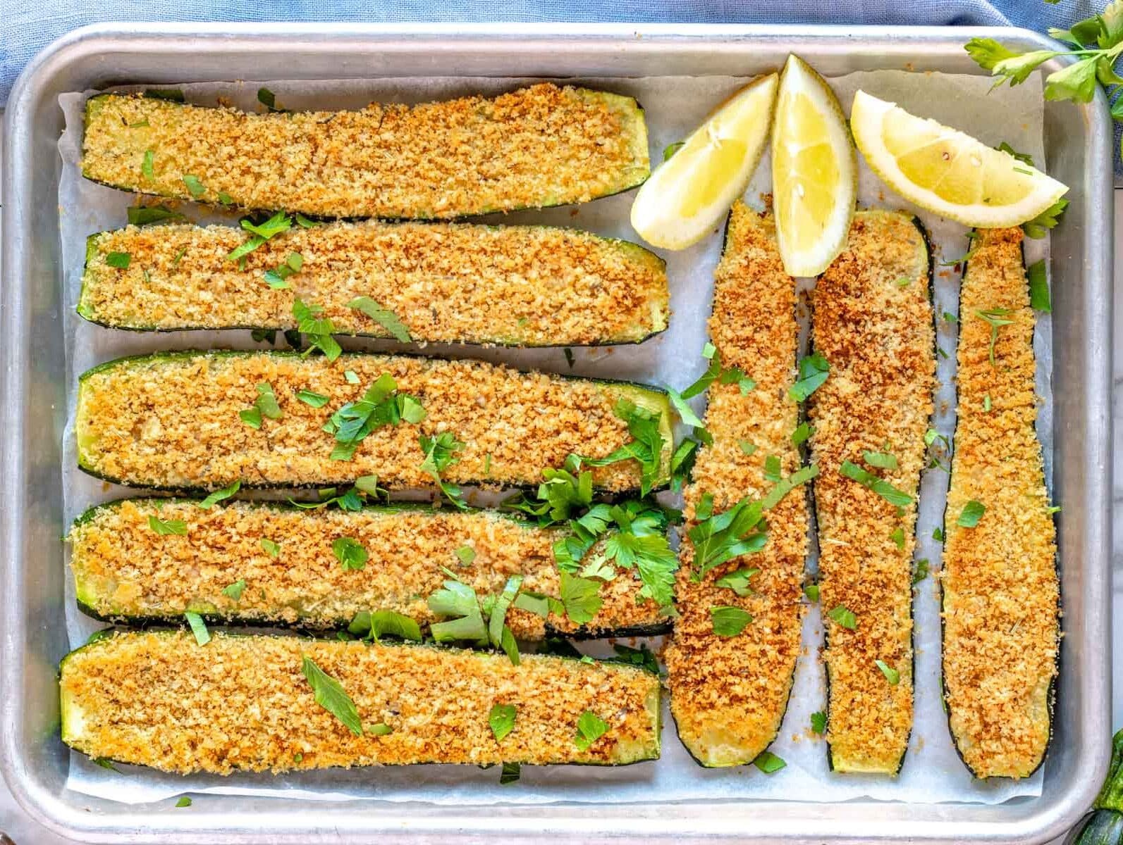roasted zucchini on a silver tray with lemon wedges