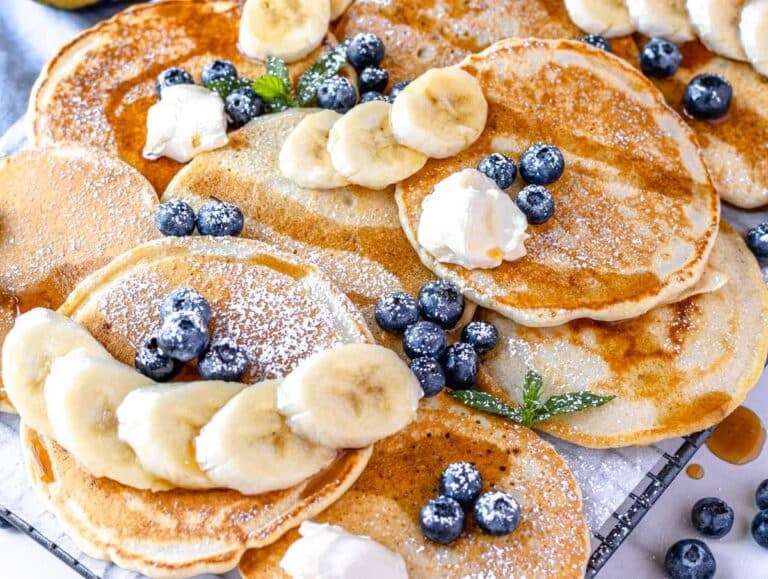 vegan pancakes on a platter with blueberries, banana, and maple syrup